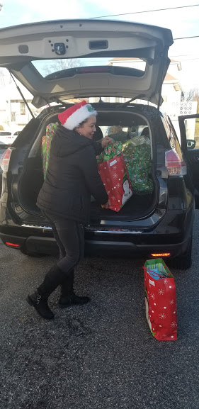 A woman in a black coat carrying gifts from a car
