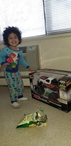 A little girl smiling and pointing to a toy car