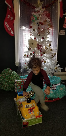 A child playing with a small toy car in front of a white Christmas tree