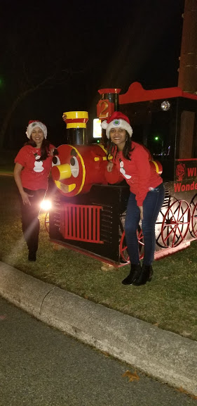 Two women wearing red shirts and Santa hats and a red train attraction