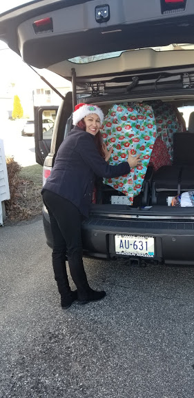 A woman wearing a Santa hat getting a big gift from the car trunk