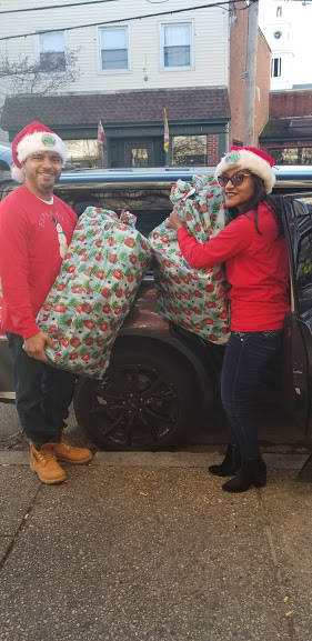 A man and a woman wearing red shirts carrying big Christmas gifts from a car