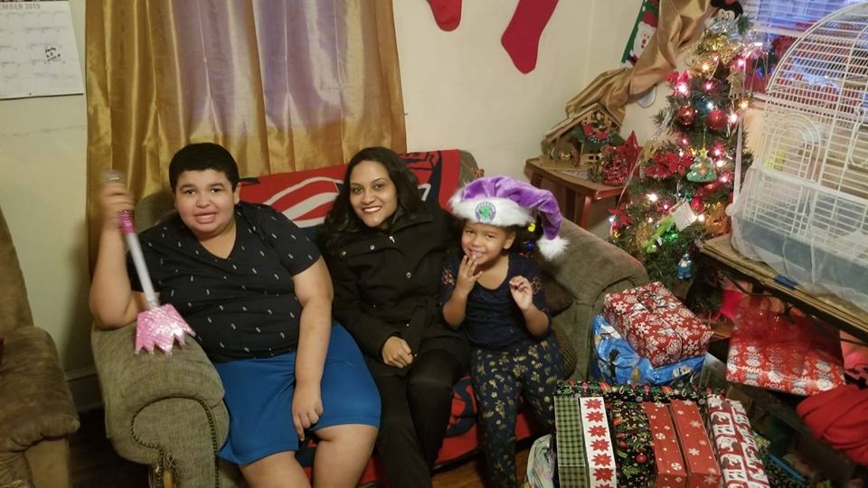 Our female staff, a boy, and a little girl wearing a purple Santa hat, all sitting on the couch