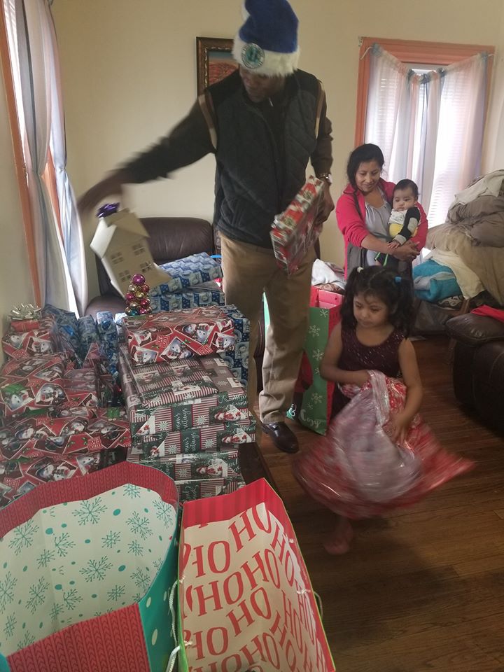 Our male staff picking gifts from the pile of presents as a little girl tries to help him; a mother and child in the back (1)