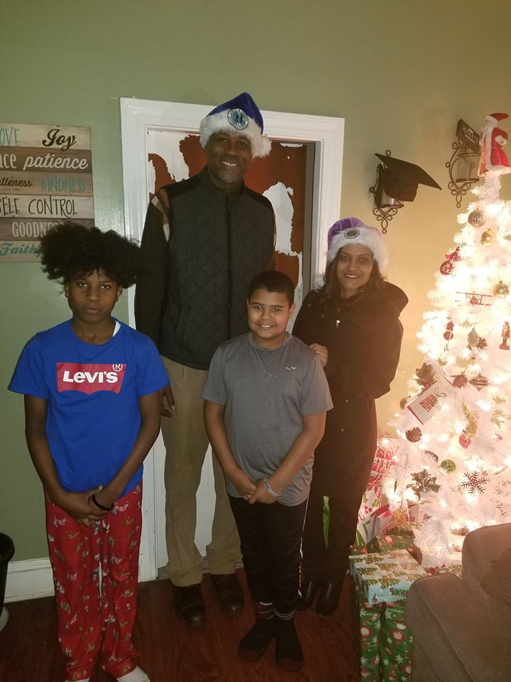 Two young boys and two of our staff (a man and a woman wearing Santa hats) standing beside a Christmas tree