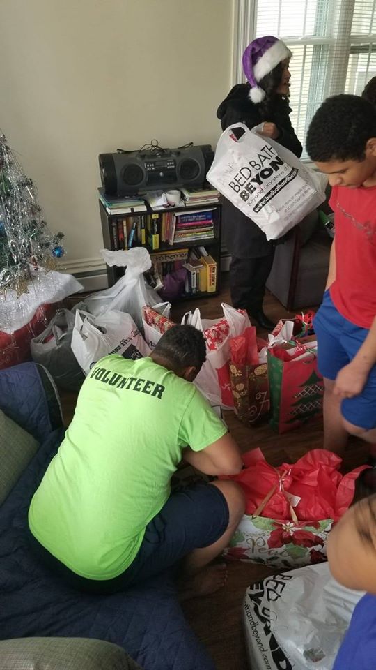 Our male staff picking gifts from the pile of presents as a little girl tries to help him; a mother and child in the back (2)