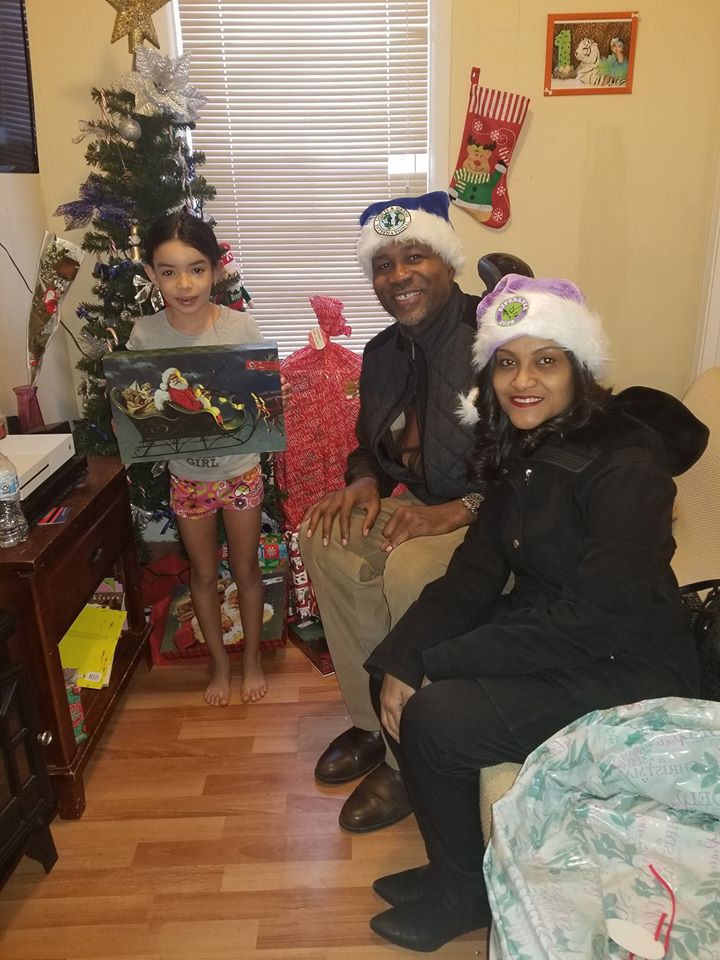 A little girl holding a toy in front of a Christmas tree with two of our staff (a man and a woman)