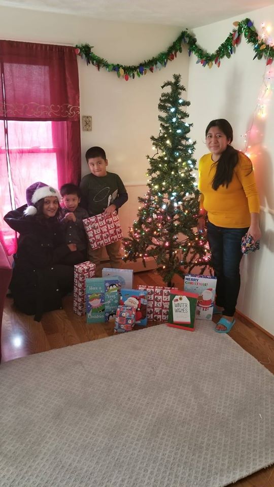 One of our staff, a woman, and two little boys in front of a Christmas tree with gifts