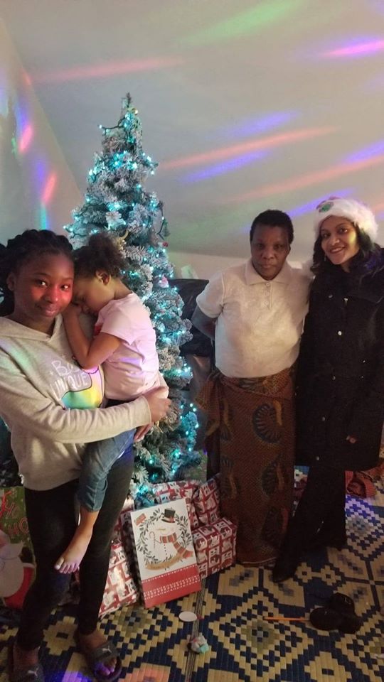 Our female staff together with a woman and two girls posing beside a Christmas tree with gifts