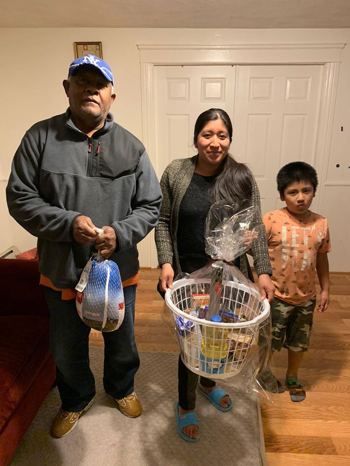 A mother, her son, and our staff holding a bag of turkey and a basket of oil, milk, and more