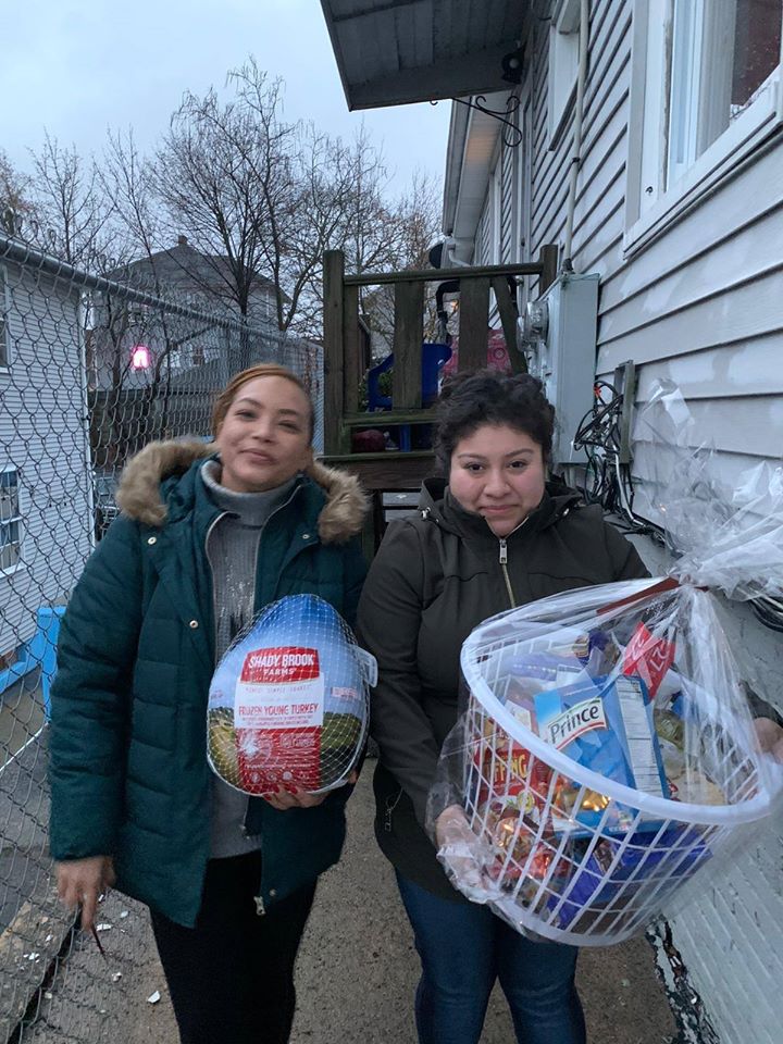 Two women outside a house and holding a bag of turkey and a basket of groceries