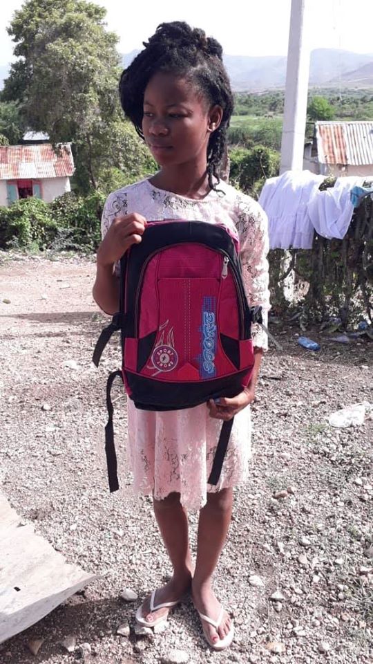 A girl wearing a pink dress holding a red and black backpack