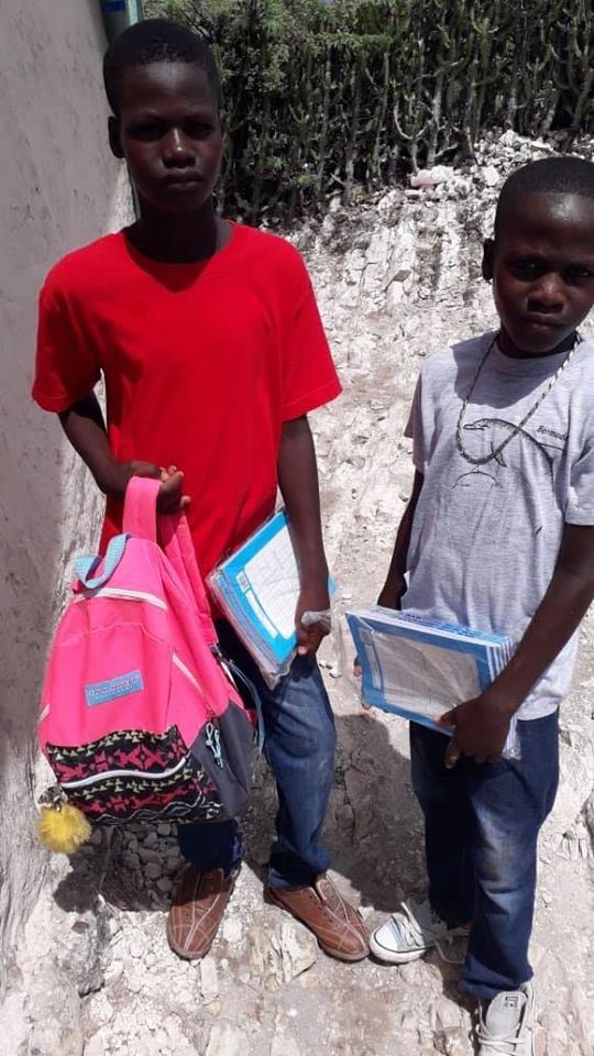 Two boys holding notebooks and a pink and black backpack