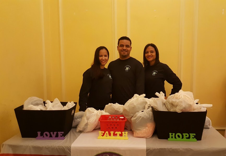 Our three staff standing at a table with a baskets of clothes in plastic bags, larger