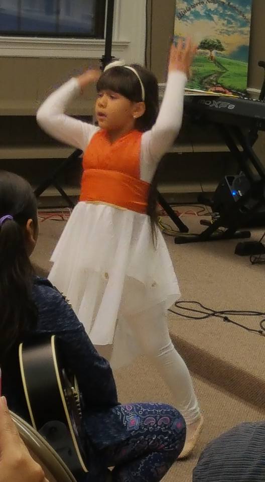 A girl with bangs wearing an orange and white dress, performing