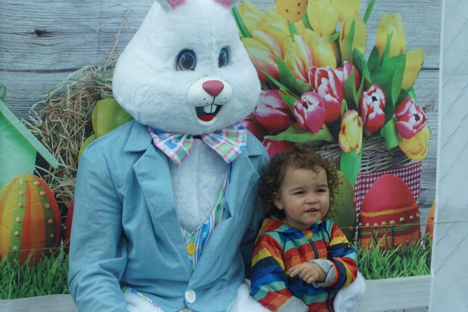 A toddler in a rainbow jacket and a bunny mascot