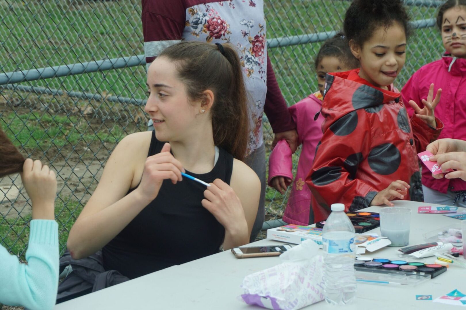 One of the artists wearing a black top and holding a blue paint brush and some kids in the background
