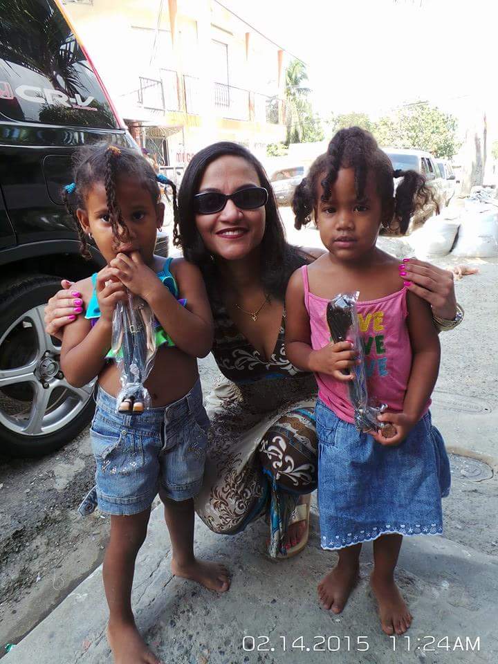 A woman and two little girls holding dolls on the road