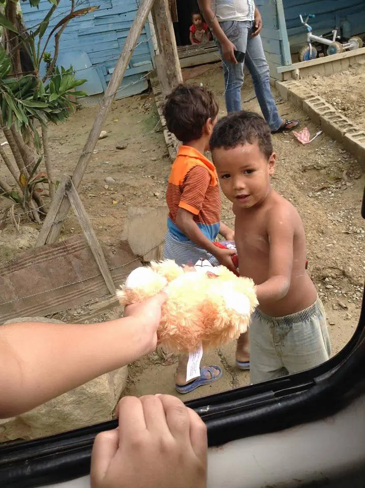 Person from inside the car giving a teddy bear to a little boy outside