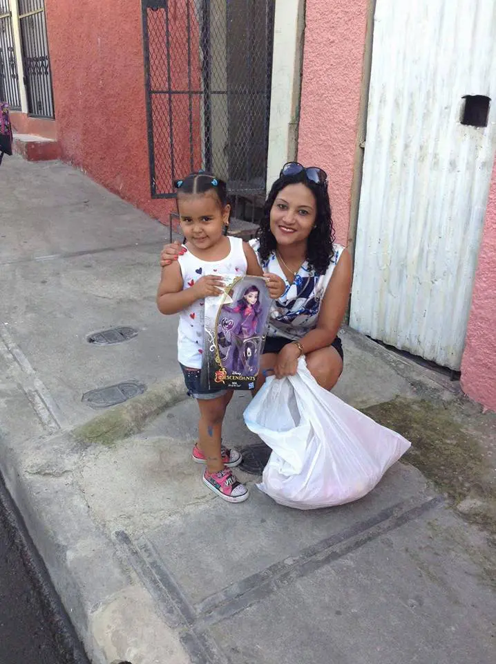 A woman with a big white plastic bag and a girl holding a doll, smiling