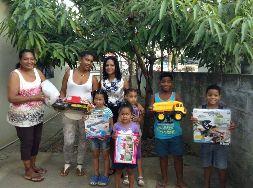 A staff, two women, and five children holding toys under a tree