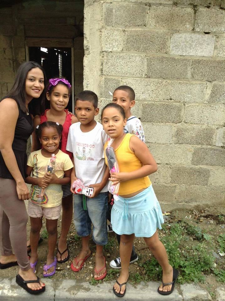 A woman and a group of children holding toys outside a house with no paint