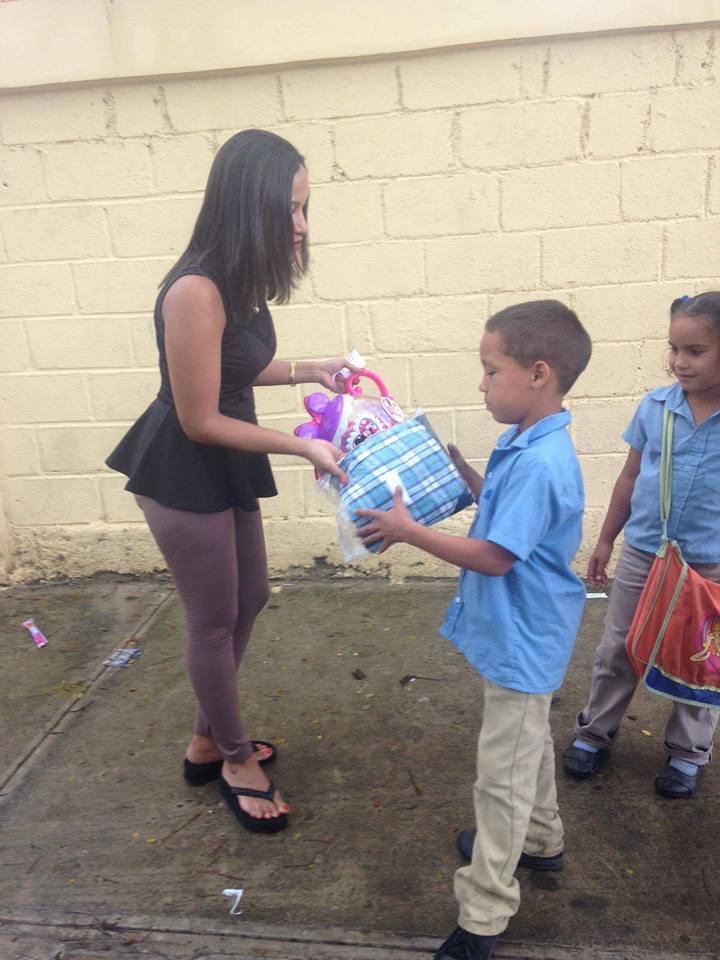 A boy and a girl in a blue school uniform receiving a pack of clothes and a toy
