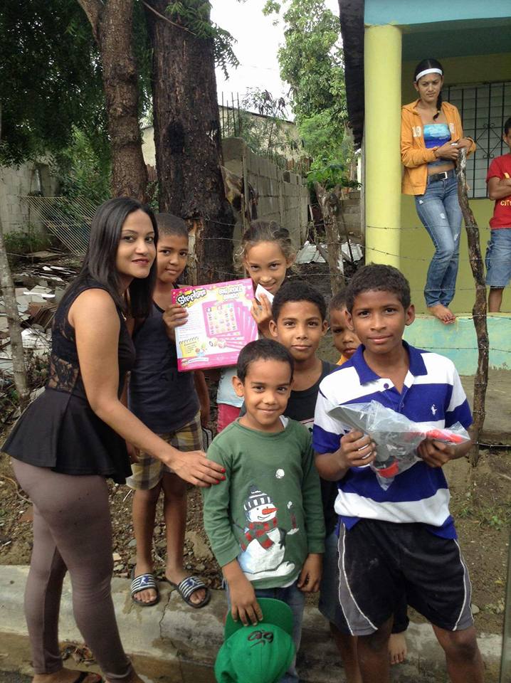 Our staff with a group of children holding toys and clothes in front of a house
