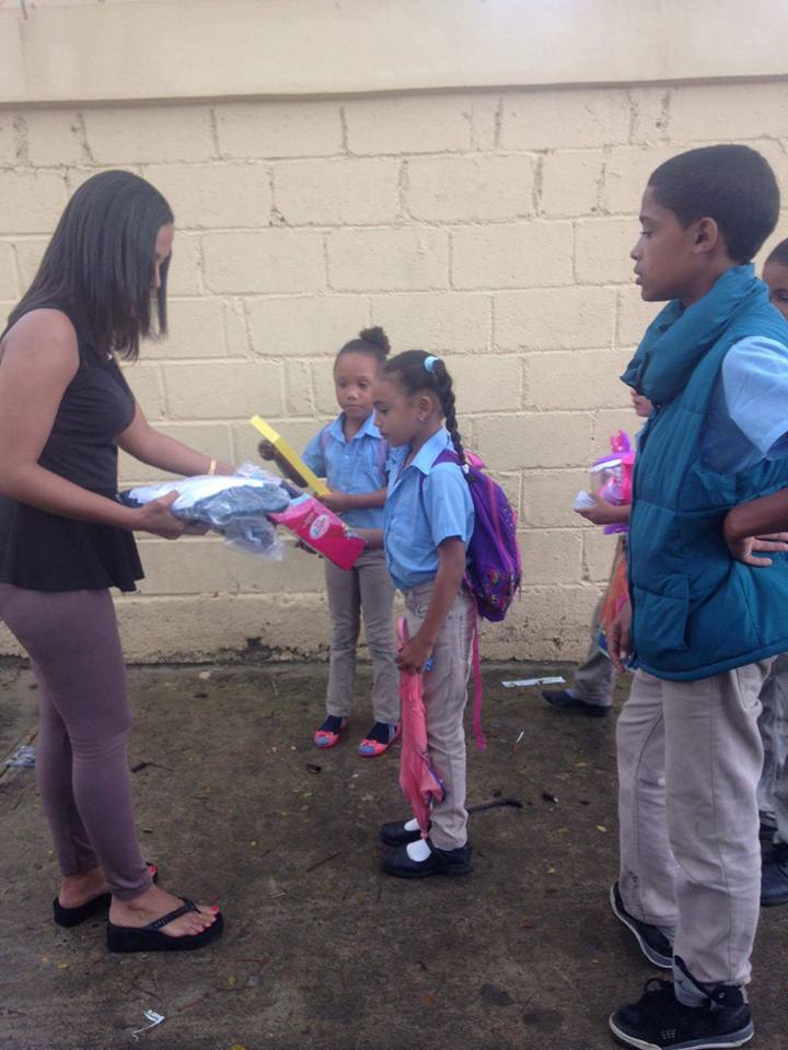Girls in blue school uniforms receiving toys from our staff; a boy looking at them