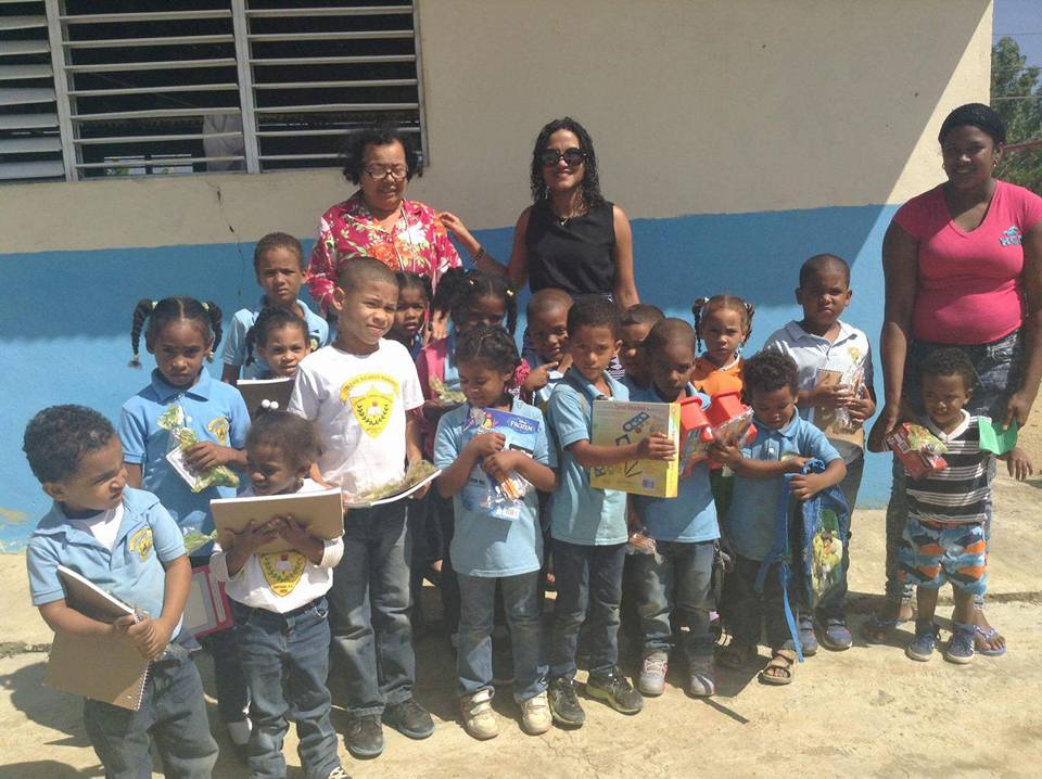 Our staff, two woman, and a big group of young children holding books and toys outside a classroom