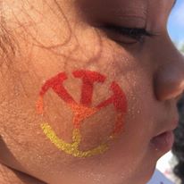 A peace sign face paint on a child’s cheek