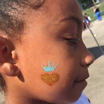 A golden heart with a blue crown on a girl’s cheek