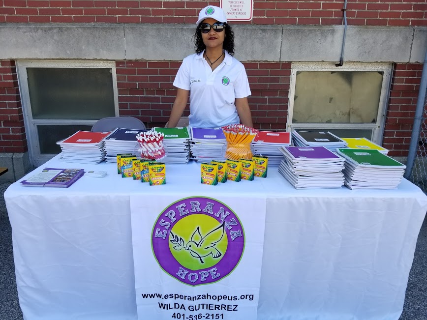 A female staff wearing sunglasses and cap posing at our table with school supplies