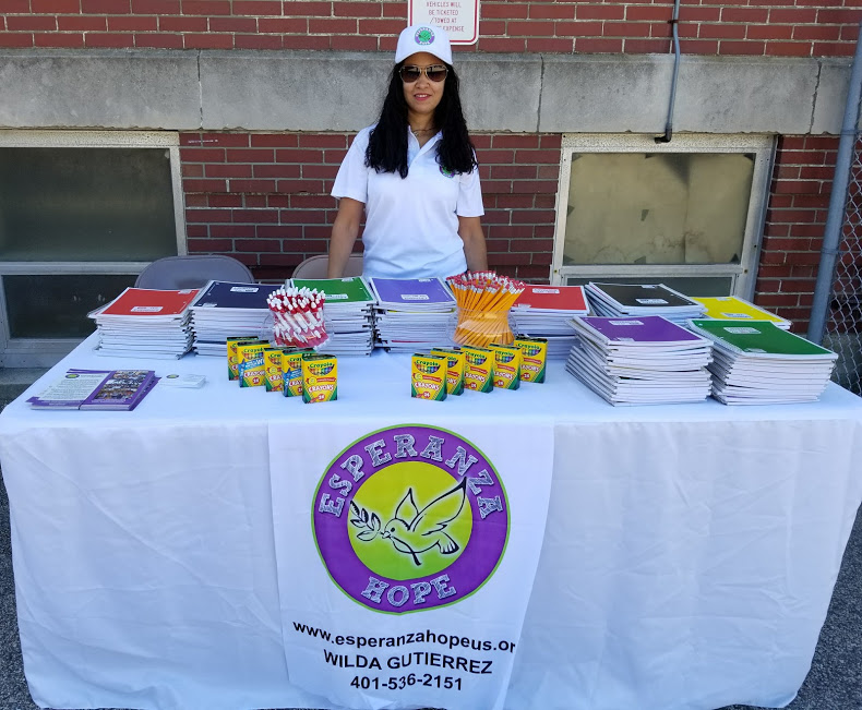 A female staff with longer hair wearing sunglasses and cap posing at our table with school supplies