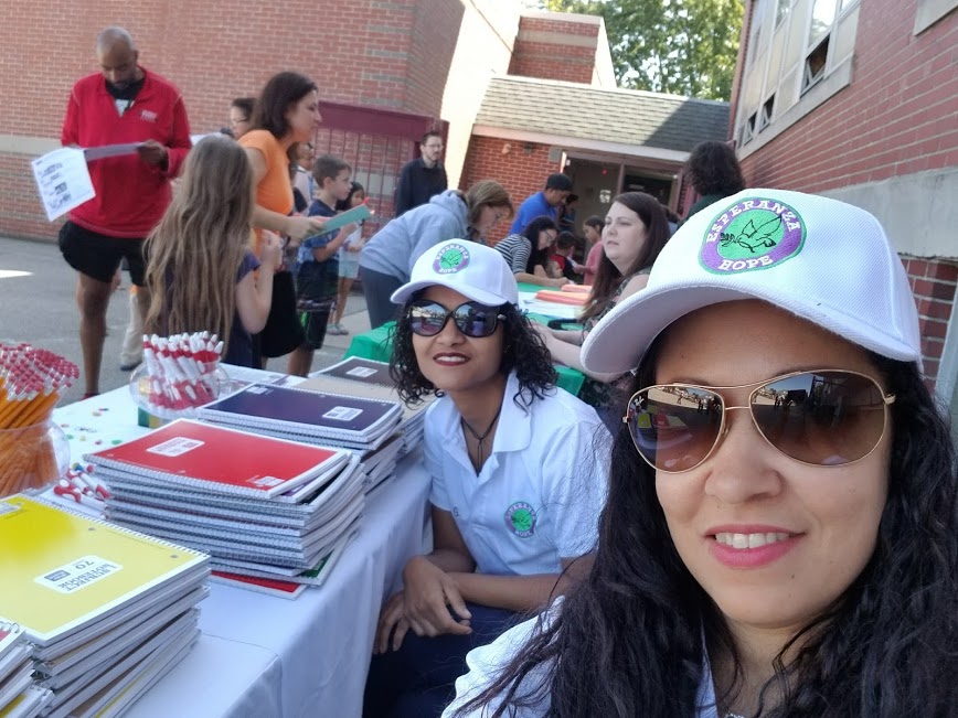 Two female staff wearing sunglasses and white cap and some parents and children filling out forms behind them