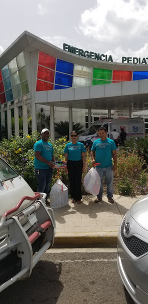 Three staff in blue shirts with two big plastic bags in front of the hospital