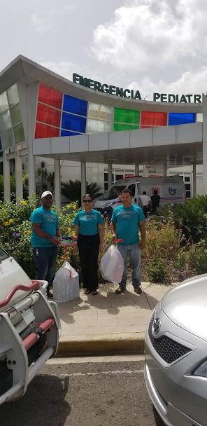 Three staff in blue shirts with two big plastic bags in front of the hospital, 2