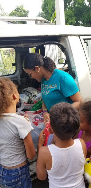 A staff getting gifts from inside the car, the children waiting outside