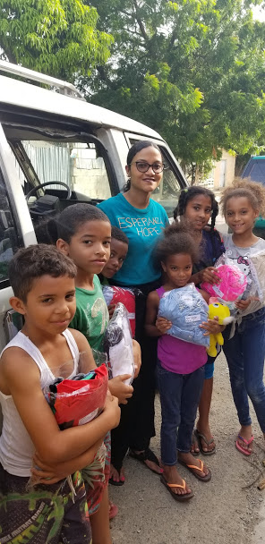 Our staff and a group of children holding packs of clothes, standing by the car