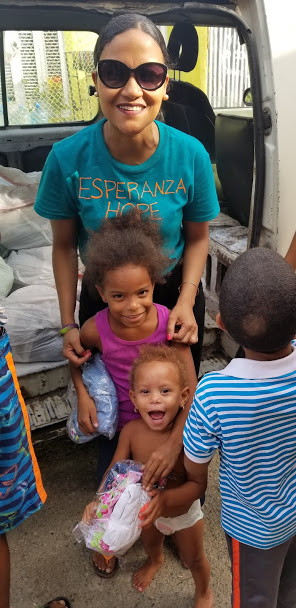 Our staff and two young children smiling and holding clothes in front of the car