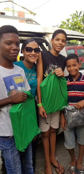 A staff and two tall boys holding a green string bag and a boy with a pack of clothes