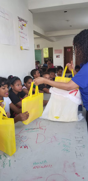 Our staff giving yellow tote bags to the children sitting at the long table
