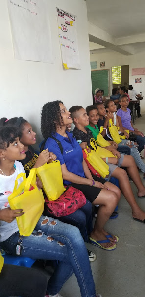 Our staff sitting with the older children with yellow tote bags at a long chair