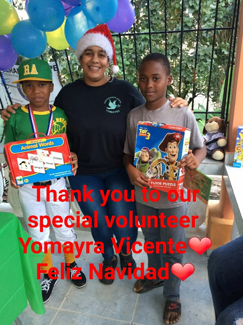 A female staff and two boys holding a box of toys; “Thanks to our special volunteer Yomayra Vicente”