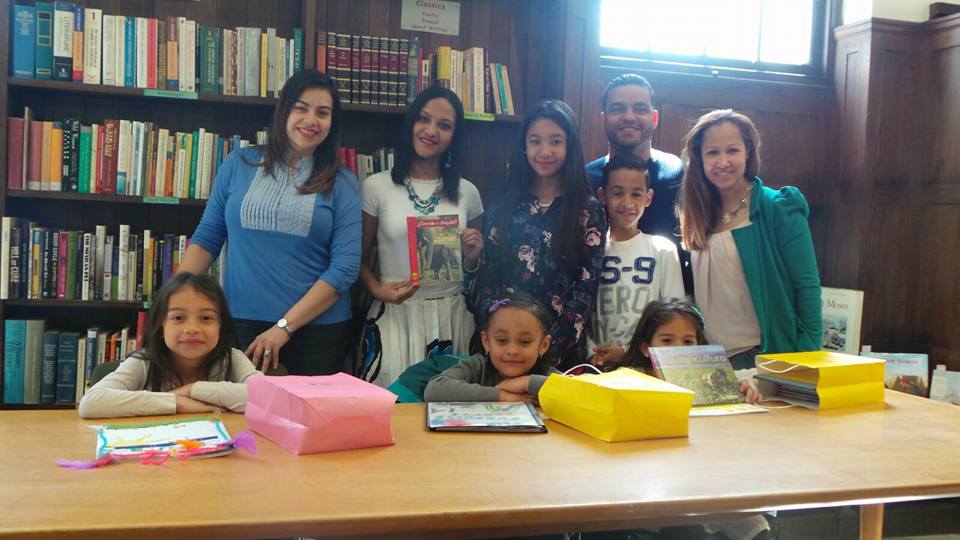 Four staff and two older children standing, and three young girls sitting at a table with books