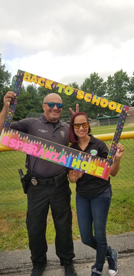 Another female staff wearing sunglasses and a police officer holding a colorful “Back to School” frame