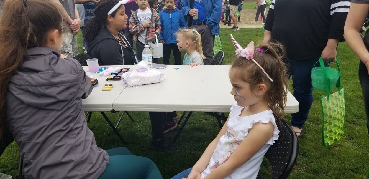 A girl with a unicorn headband sitting for the face paint