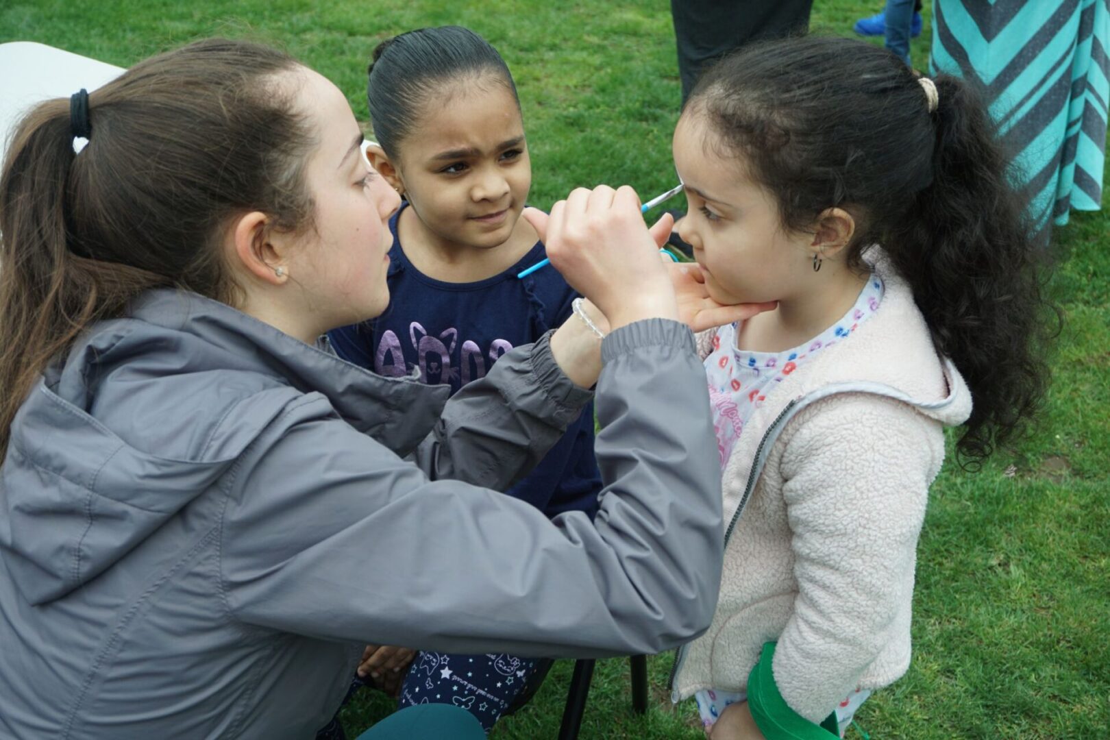 A girl sitting and watching another girl being face painted