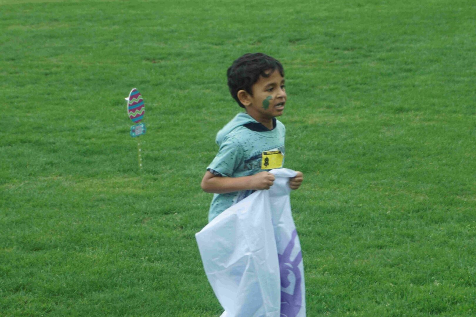 A boy in a green shirt and face paint of a turtle, playing in a sack race