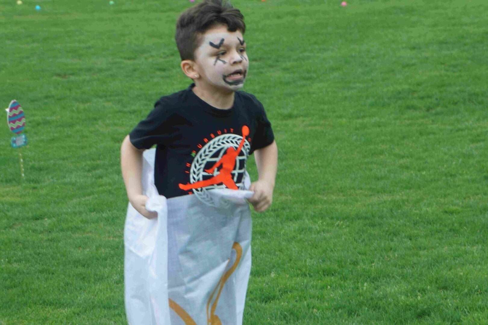 A boy in black shirt and face paint playing in a sack race